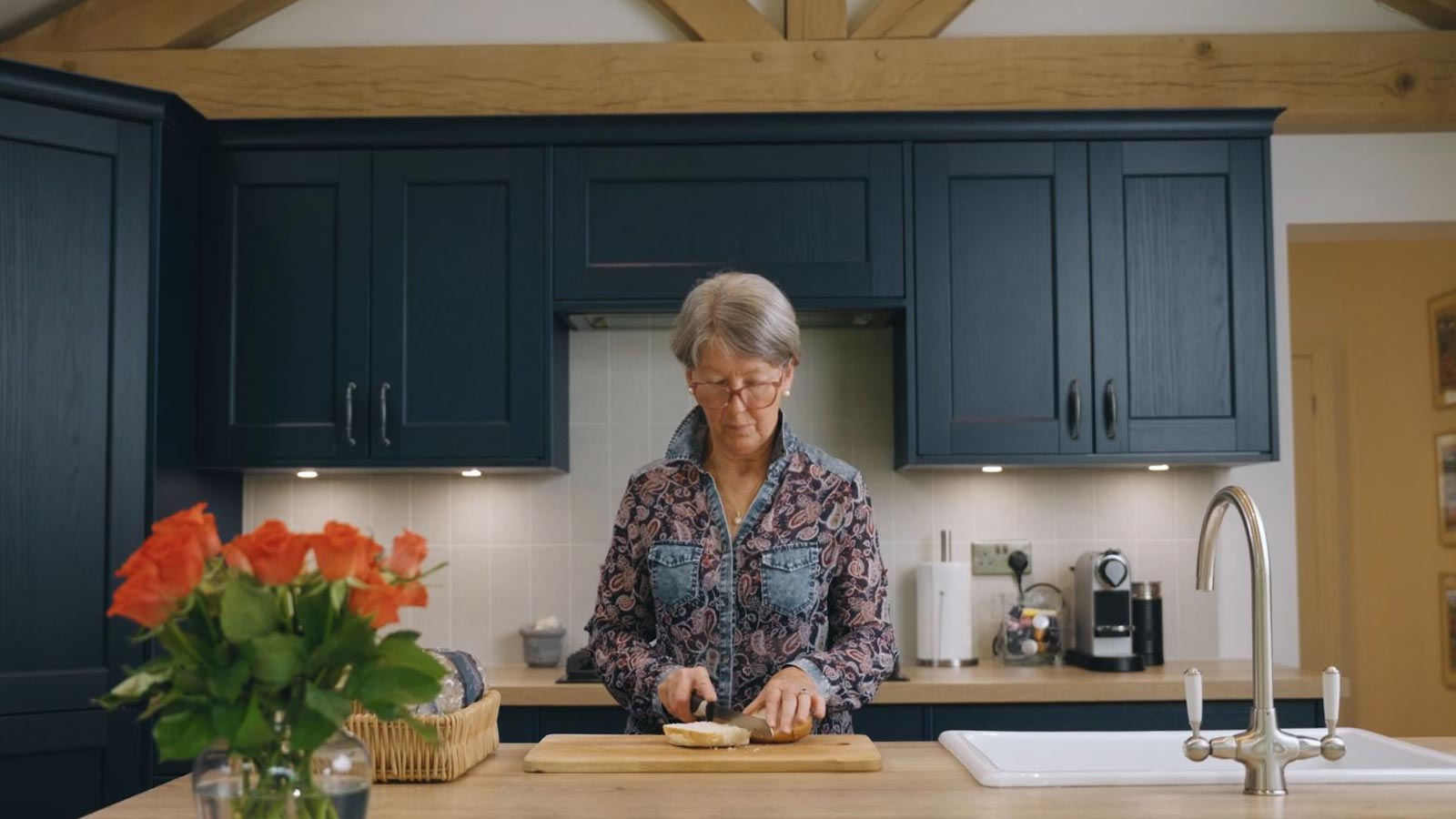 Edwina in her dark blue classic kitchen cutting bread