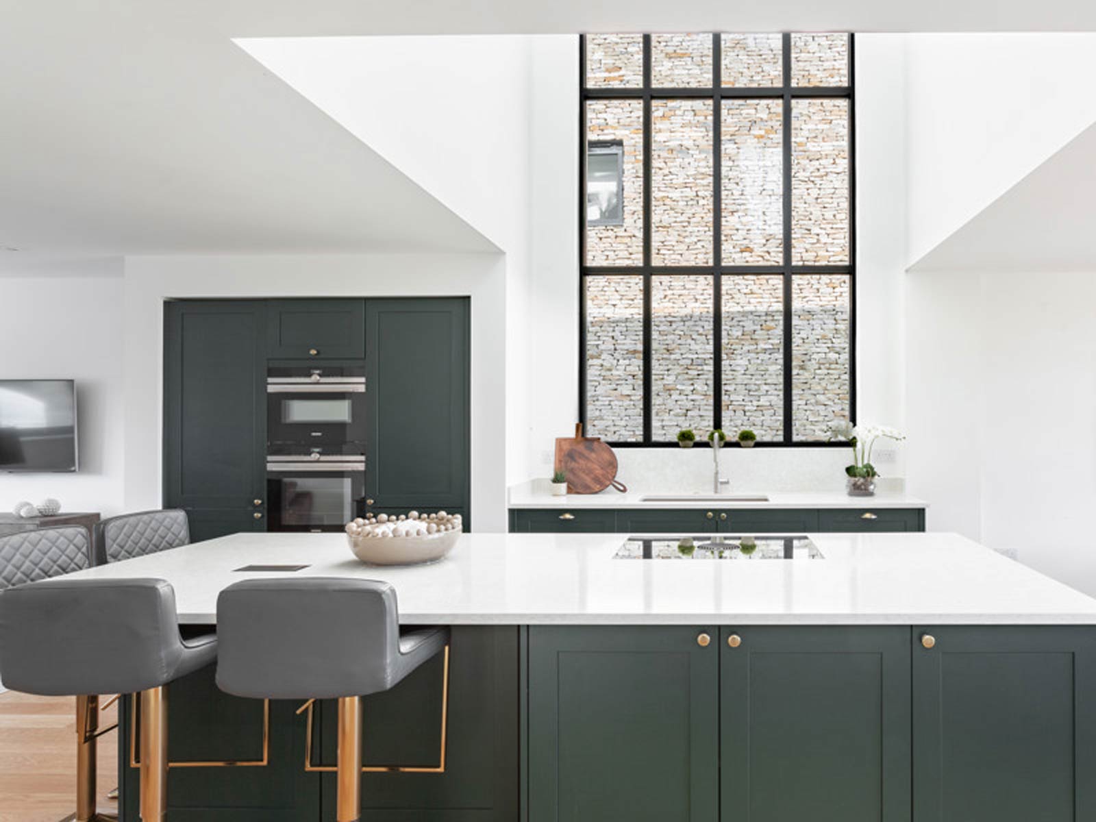 A perfect kitchen with a high, bright ceiling and dark green cupboards