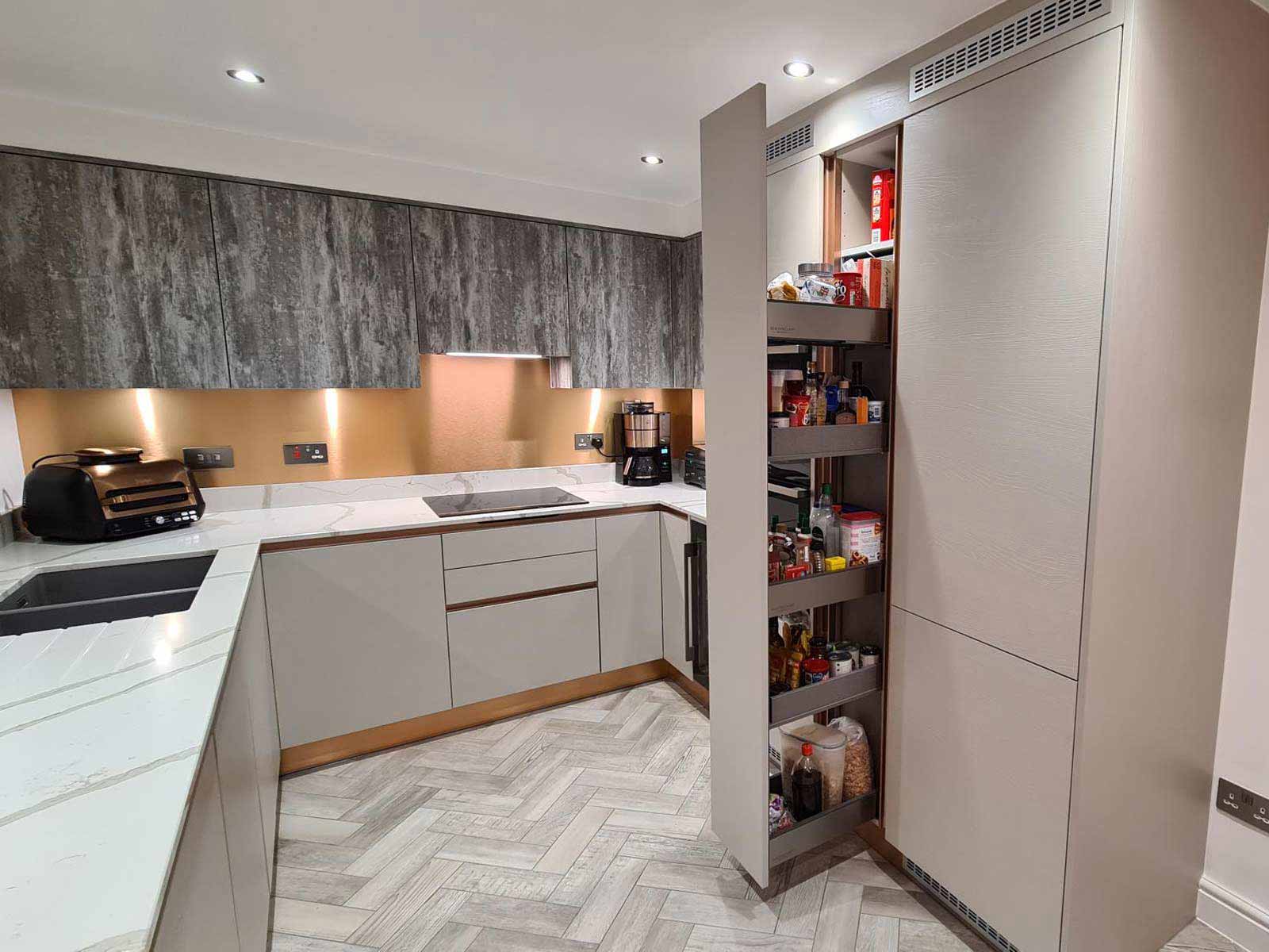 A light grey cashmere kitchen with wood-effect units and a gold splashback
