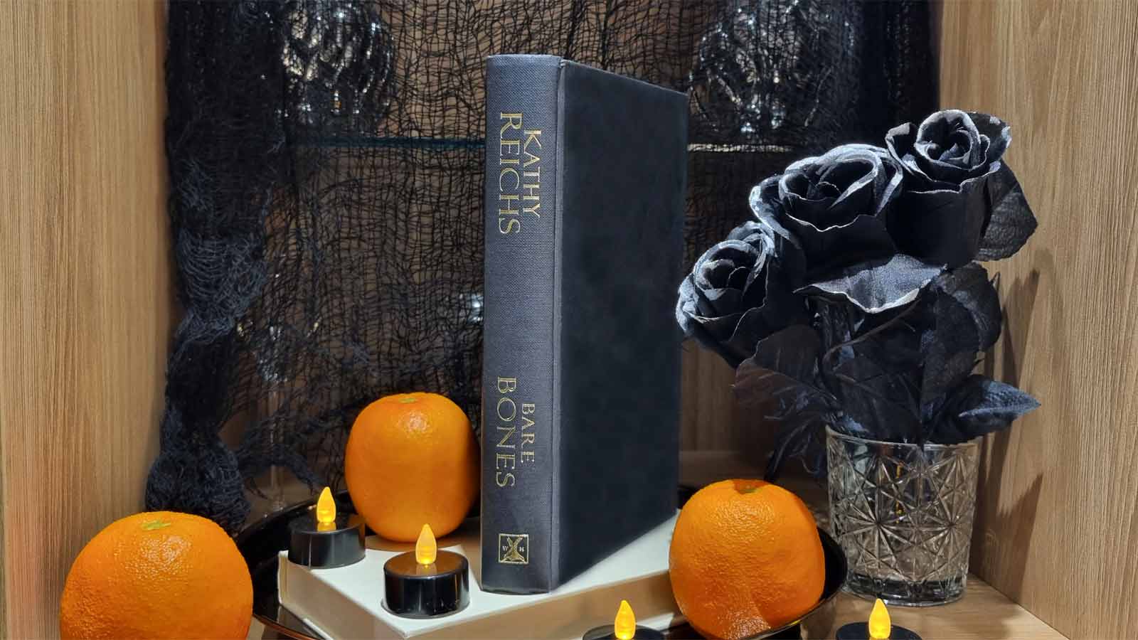 A horror book with black Halloween roses, candles and oranges