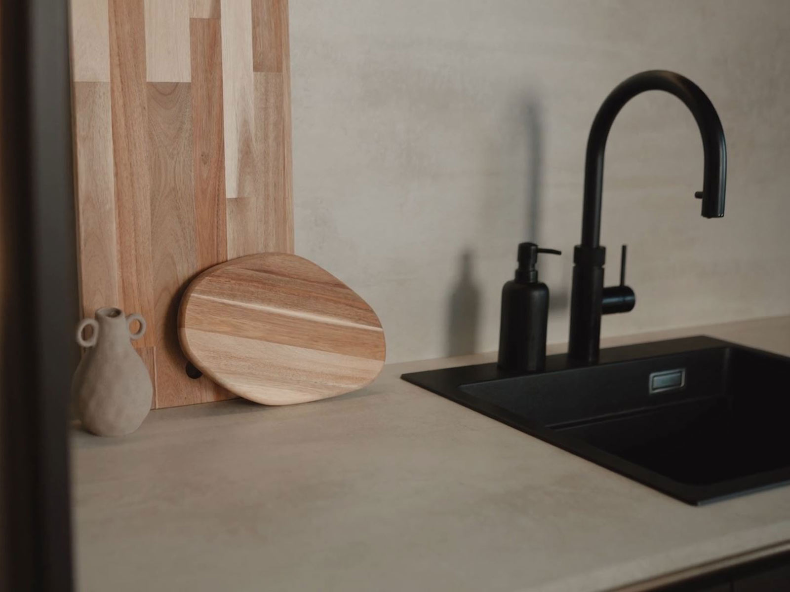 A modern kitchen worktop with a black sink and wooden chopping boards