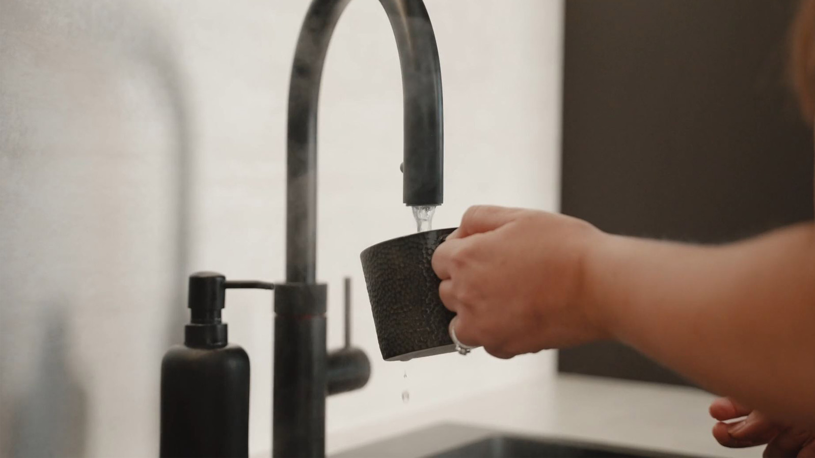 A black Quooker tap with stone countertops that create a rustic kitchen feel