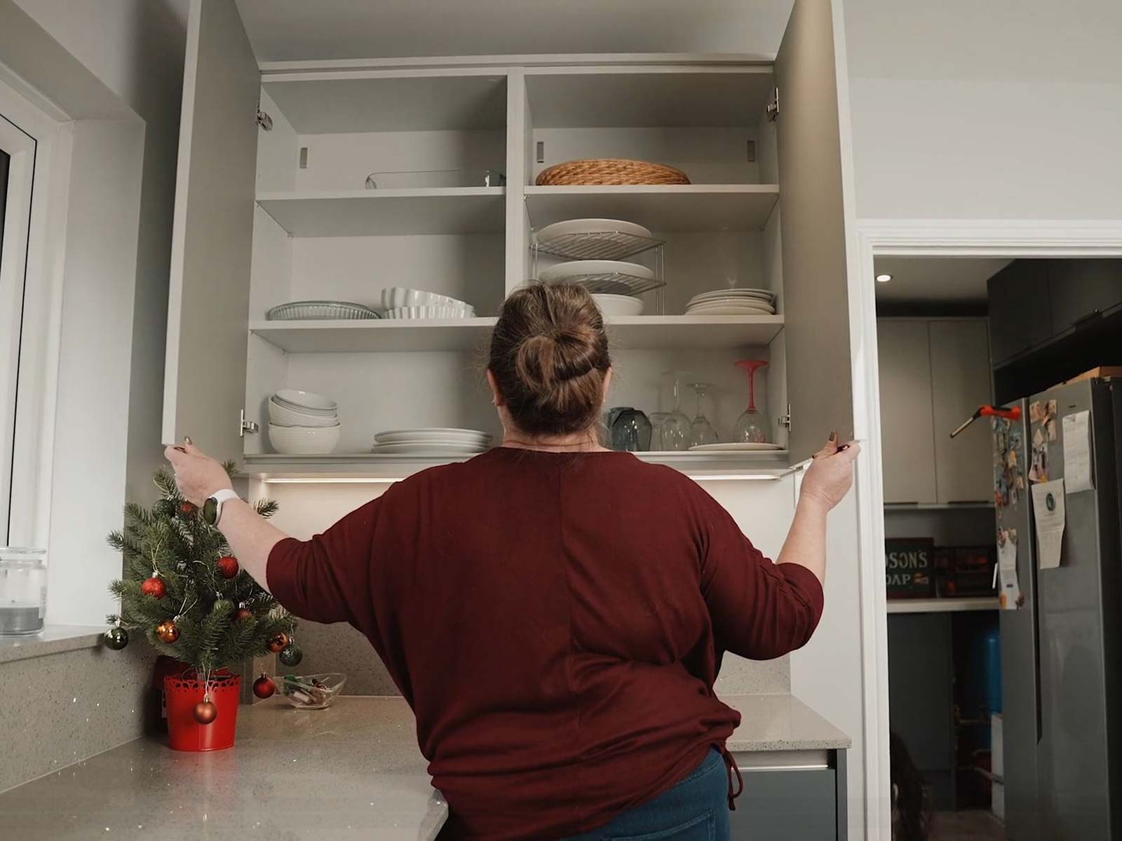 Gail opening white gloss handleless kitchen cupboards in a corner kitchenette