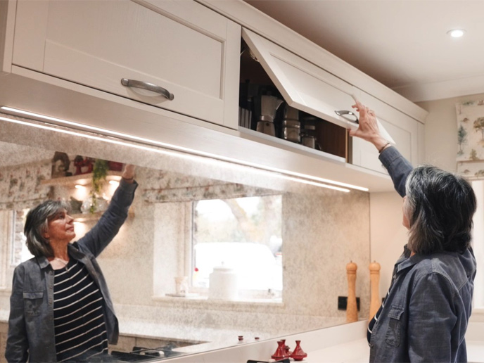 Rita opening an overhead kitchen cabinet in an open plan kitchen diner