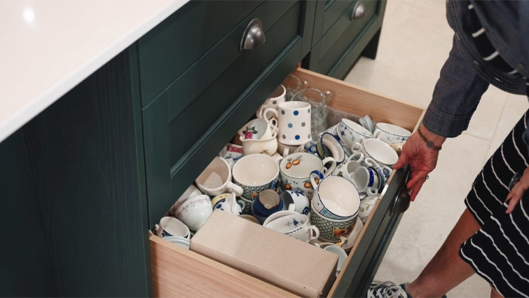 A deep drawer holding mugs in a kitchen family room with an open concept