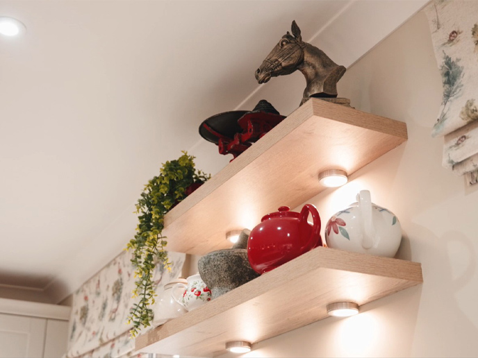 Open kitchen shelving holding a plant, figurines and teapots
