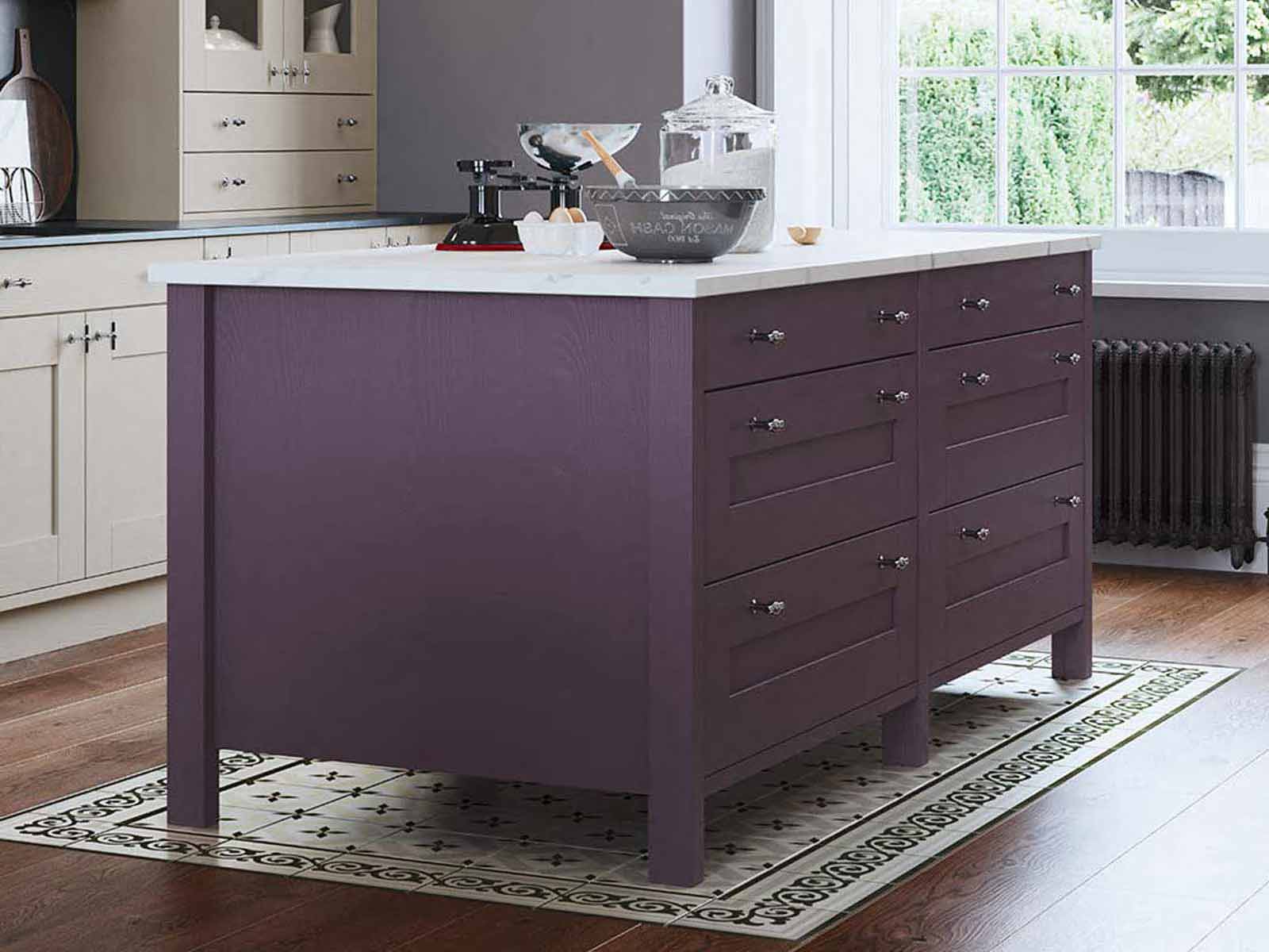 A purple kitchen island with a while marble worktop and ivory cabinets