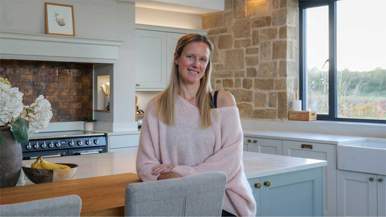 Anna in her high ceiling kitchen in front of her kitchen feature wall