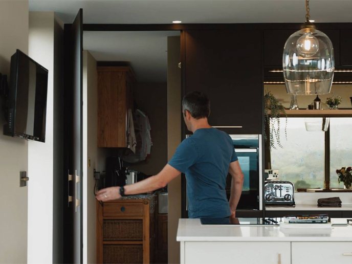 A man showing a secret room door built into his kitchen larder units